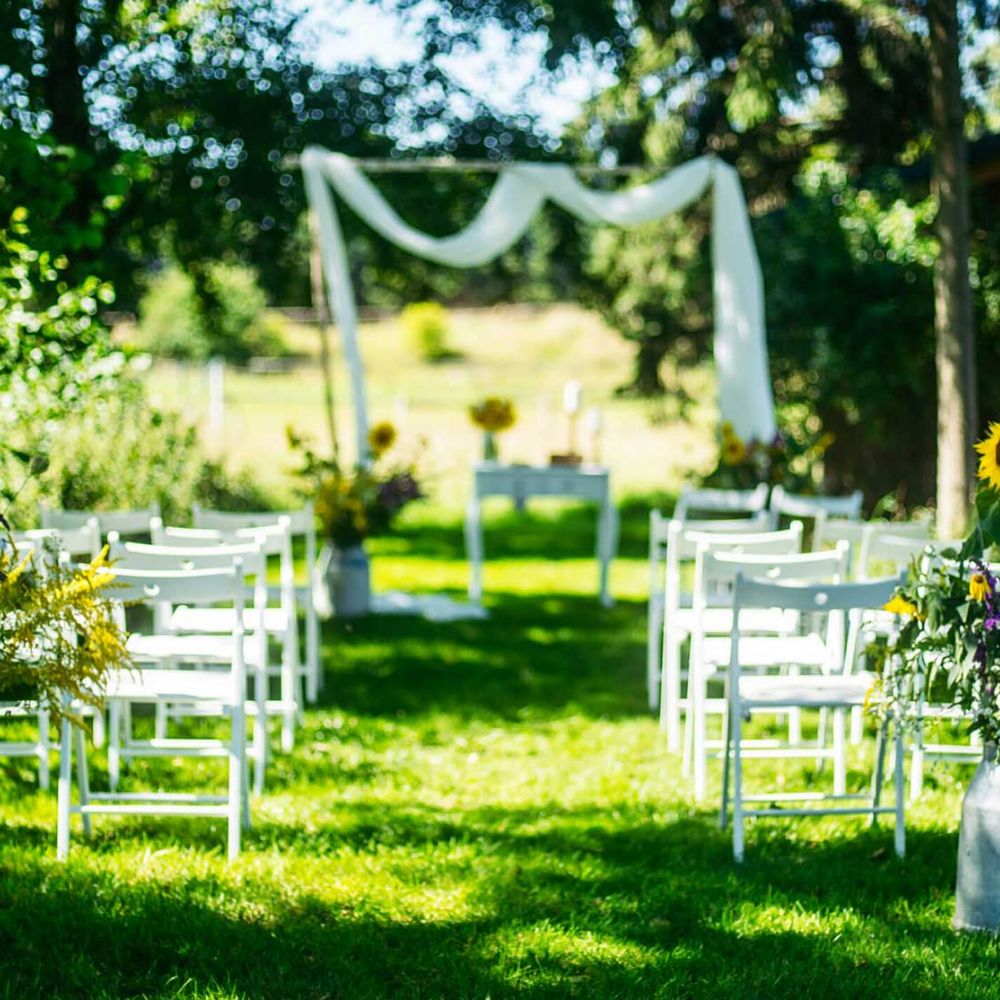 Blick in den Garten, Bestuhlung für Hochzeitsgesellschaft und Traubogen im Hintergrund, Blumendeko