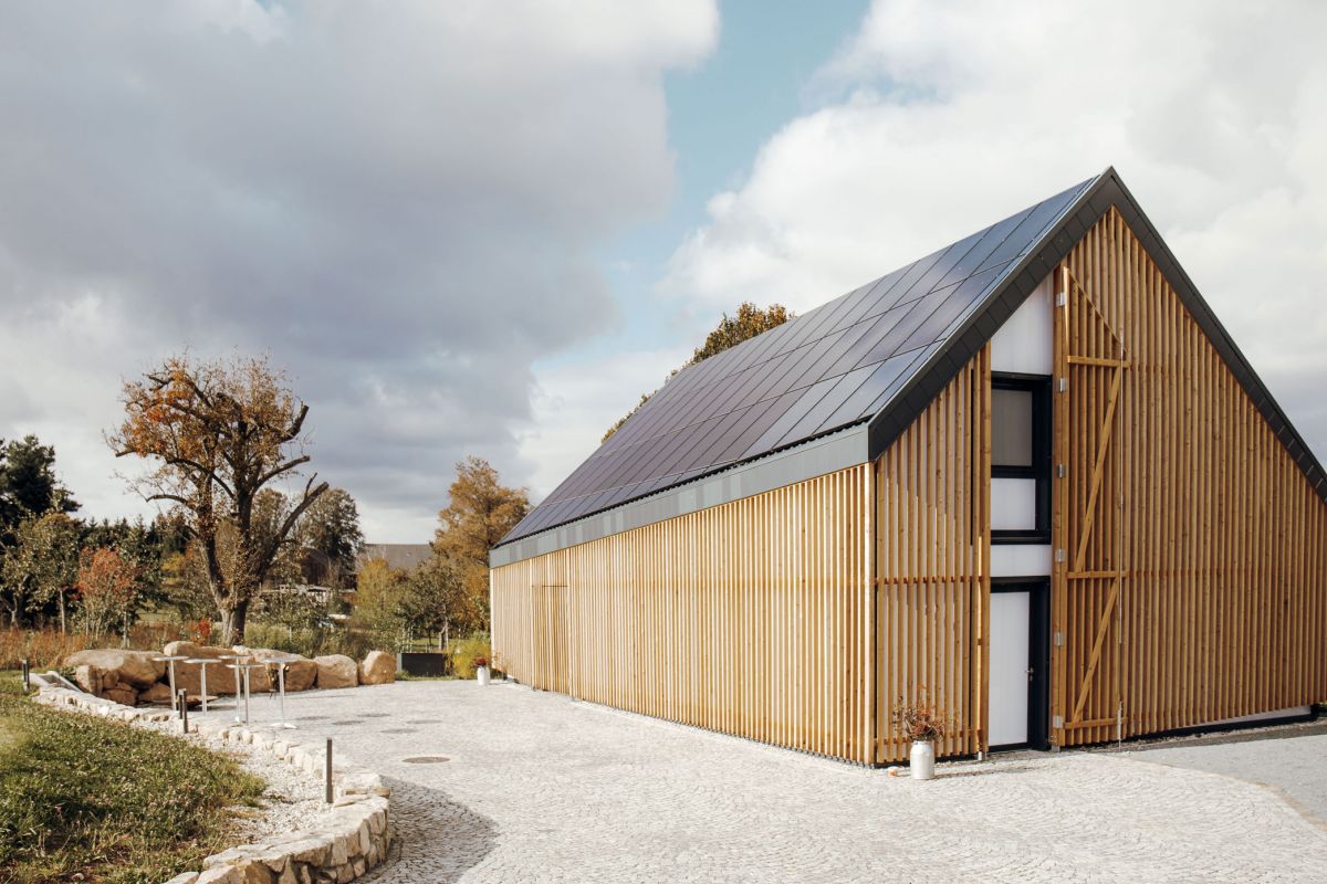 Terra.Hub: Modernes Haus mit Solarpaneelen auf dem Dach und Holzvertäfelung, im Hintergrund Himmel mit Wolken
