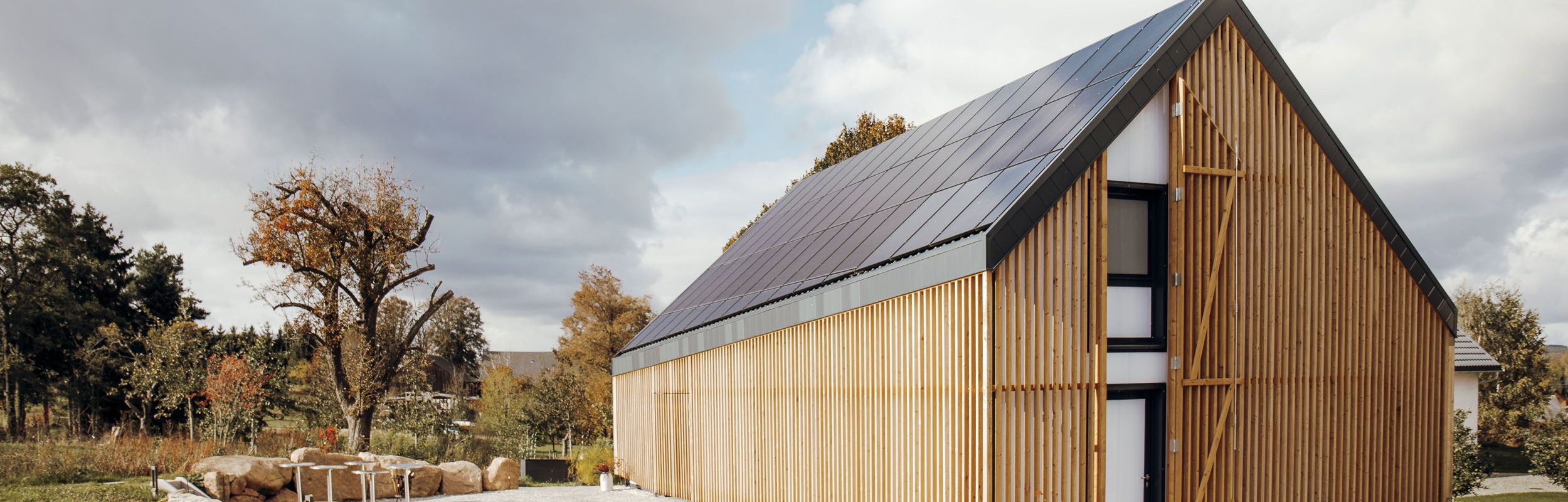Terra.Hub: Modernes Haus mit Solarpaneelen auf dem Dach und Holzvertäfelung, im Hintergrund Himmel mit Wolken