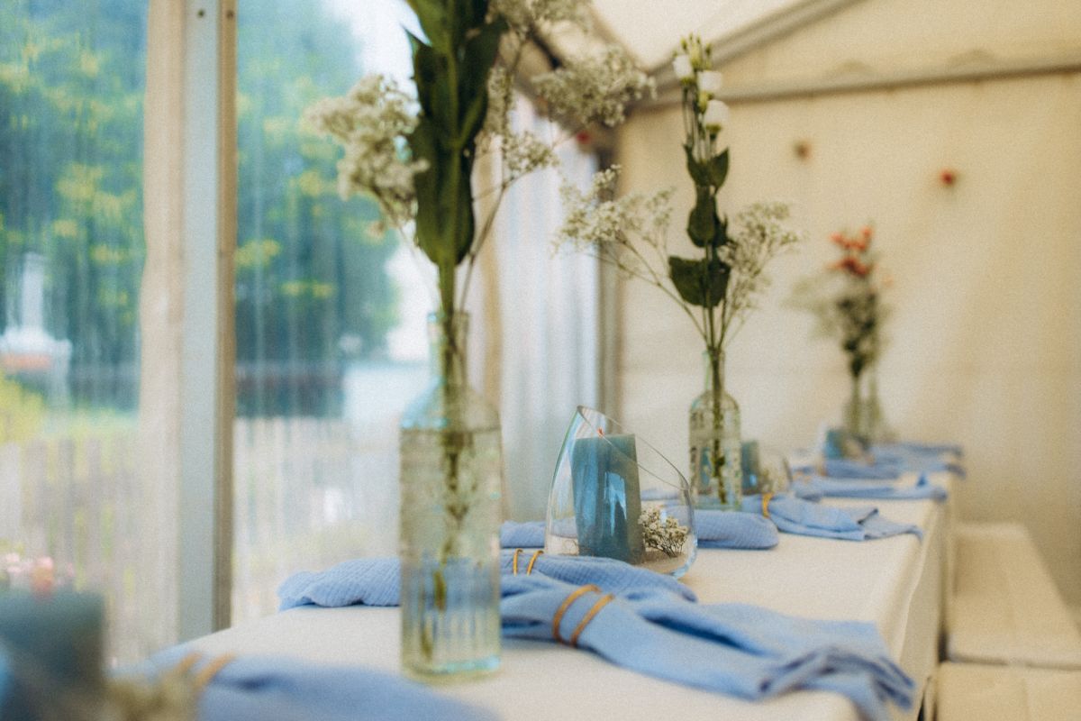 In einem Pavillon stehender weißer Tisch, darauf blaue Servietten und Blumen in Vasen.