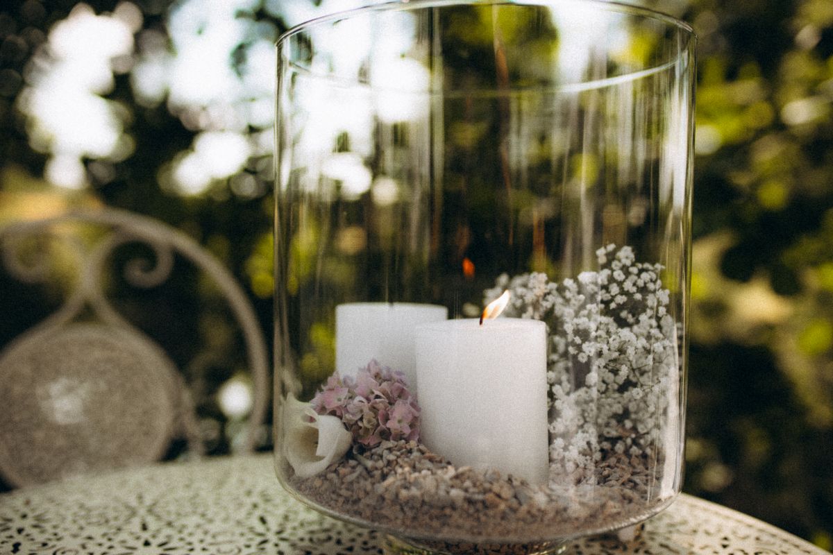 Großes Kerzenglas mit weißer, brennender Kerze und Blumen, Natur im Hintergrund