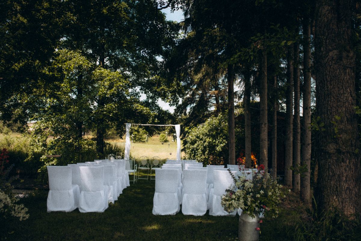 weißer Traubogen im Wald, davor weiße Stühle für die Hochzeitsgesellschaft