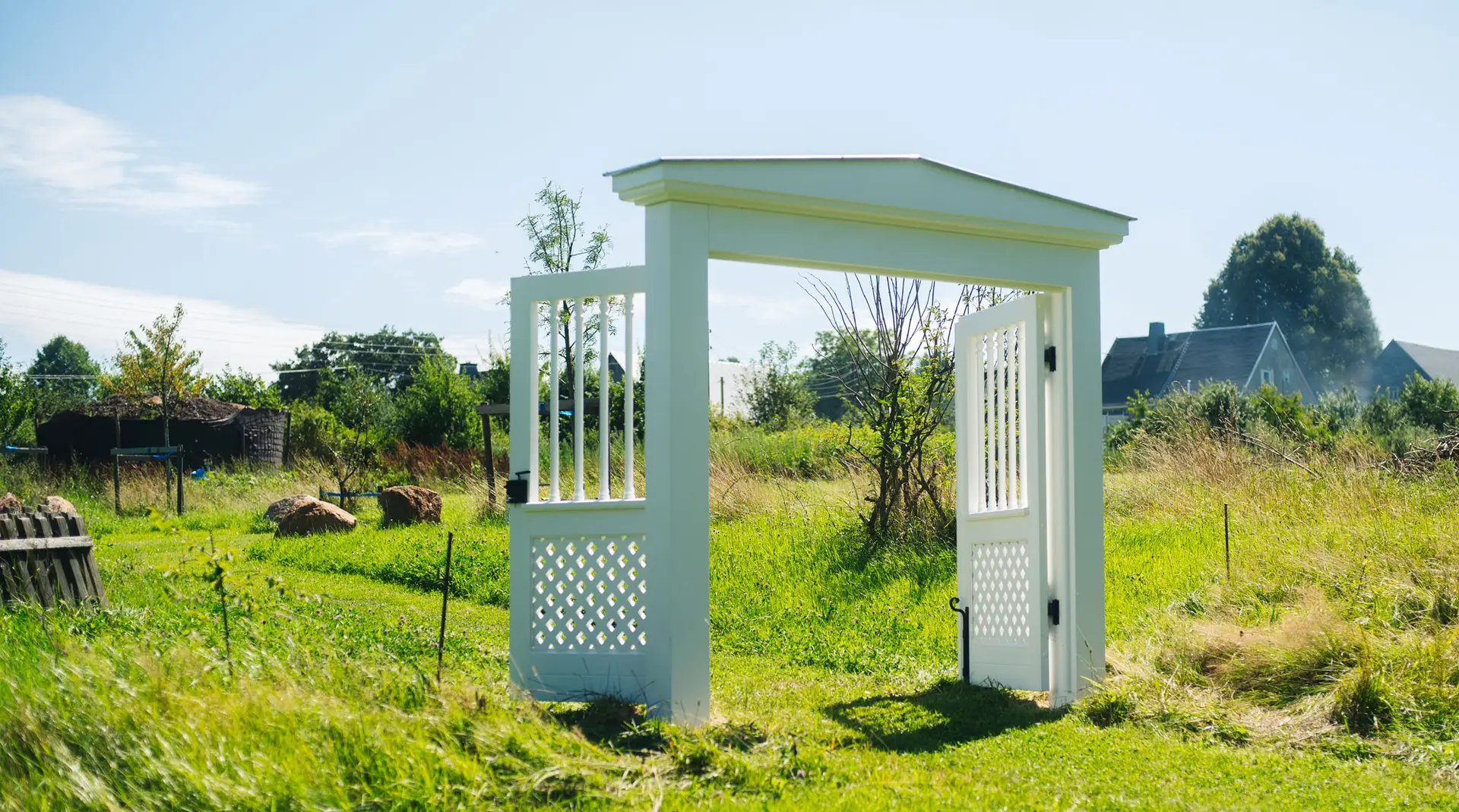 weißes Holztor mit großen Flügeltüren auf einer grünen Wiese im Terra.Garden