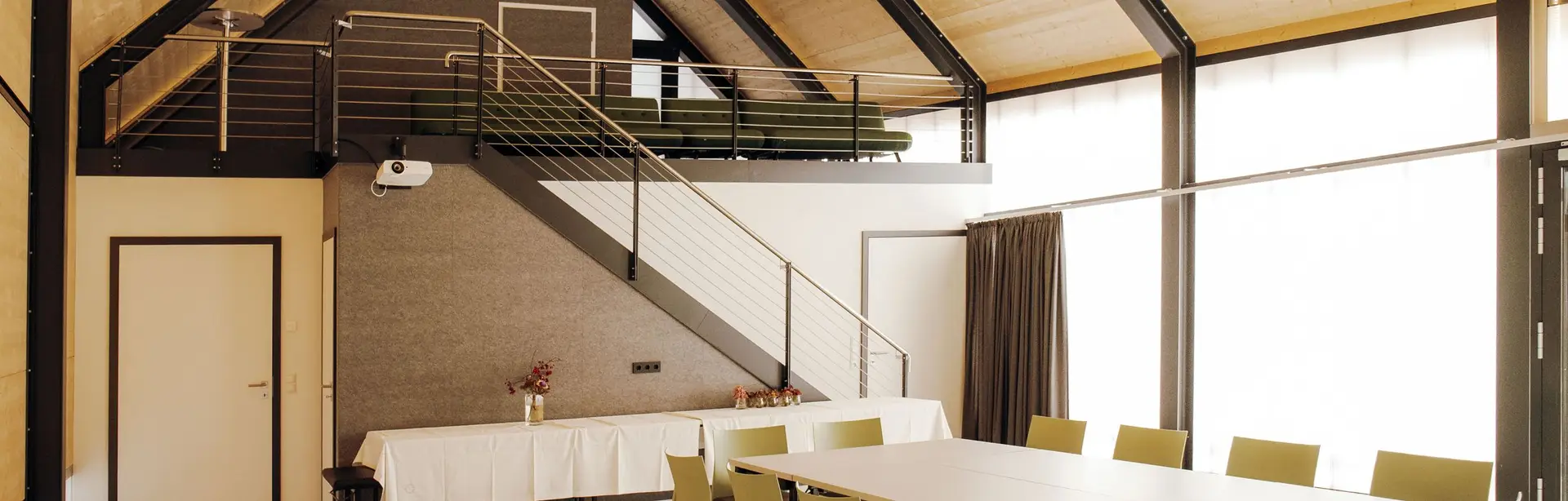 Innenansicht Terra.Hub: großer Tisch mit Stühlen im Vordergrund, dahinter Treppe zur Galerie