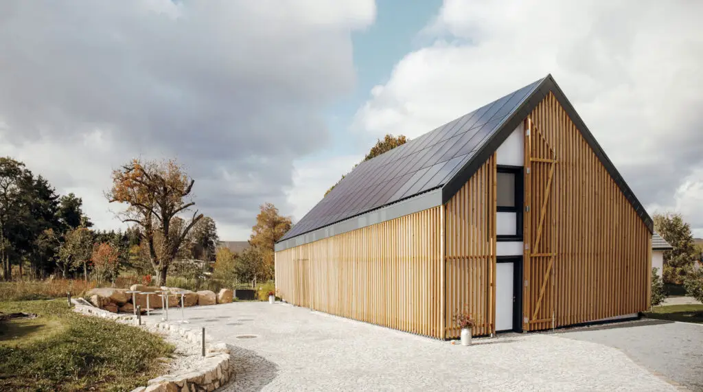 Terra.Hub: Modernes Haus mit Solarpaneelen auf dem Dach und Holzvertäfelung, im Hintergrund Himmel mit Wolken