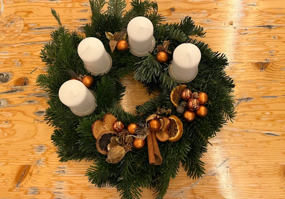 Adventskranz mit vier weißen Kerzen und orangefarbenen Blüten